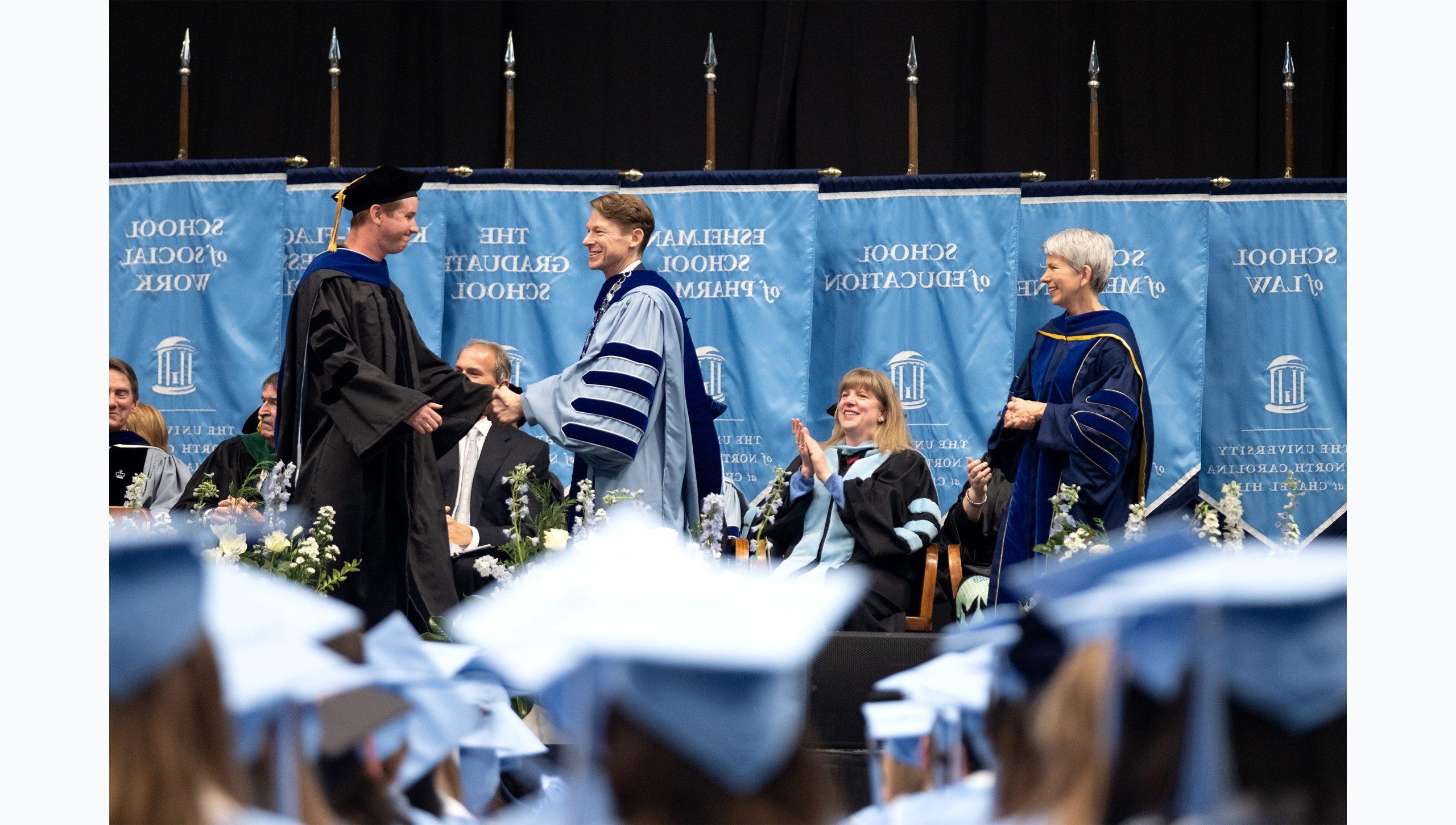 A graduate student shaking Lee H. Roberts' hand on stage at U.N.C. Chapel Hill's Winter Commencement.